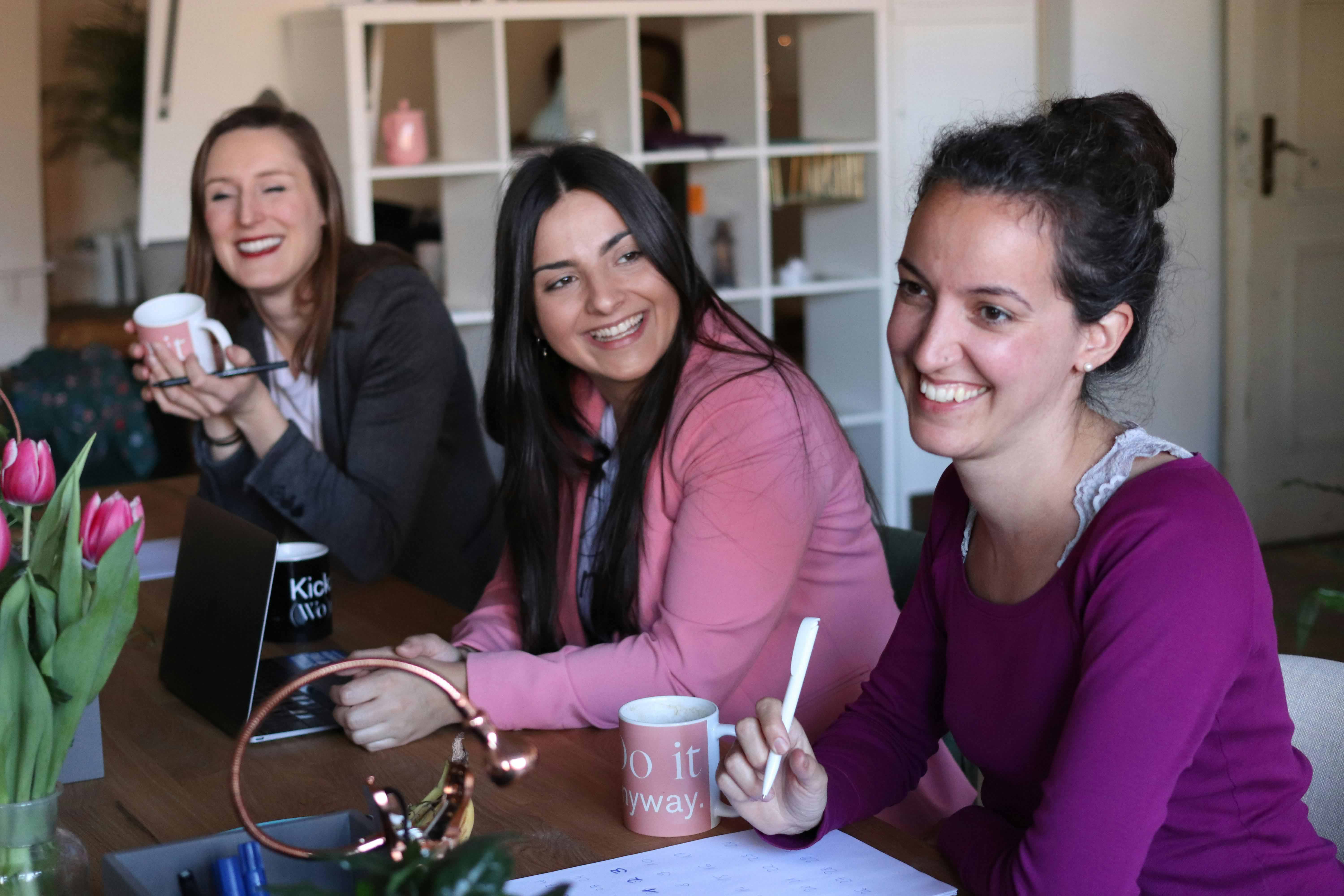 Three women smiling and enjoying coffee together at a table