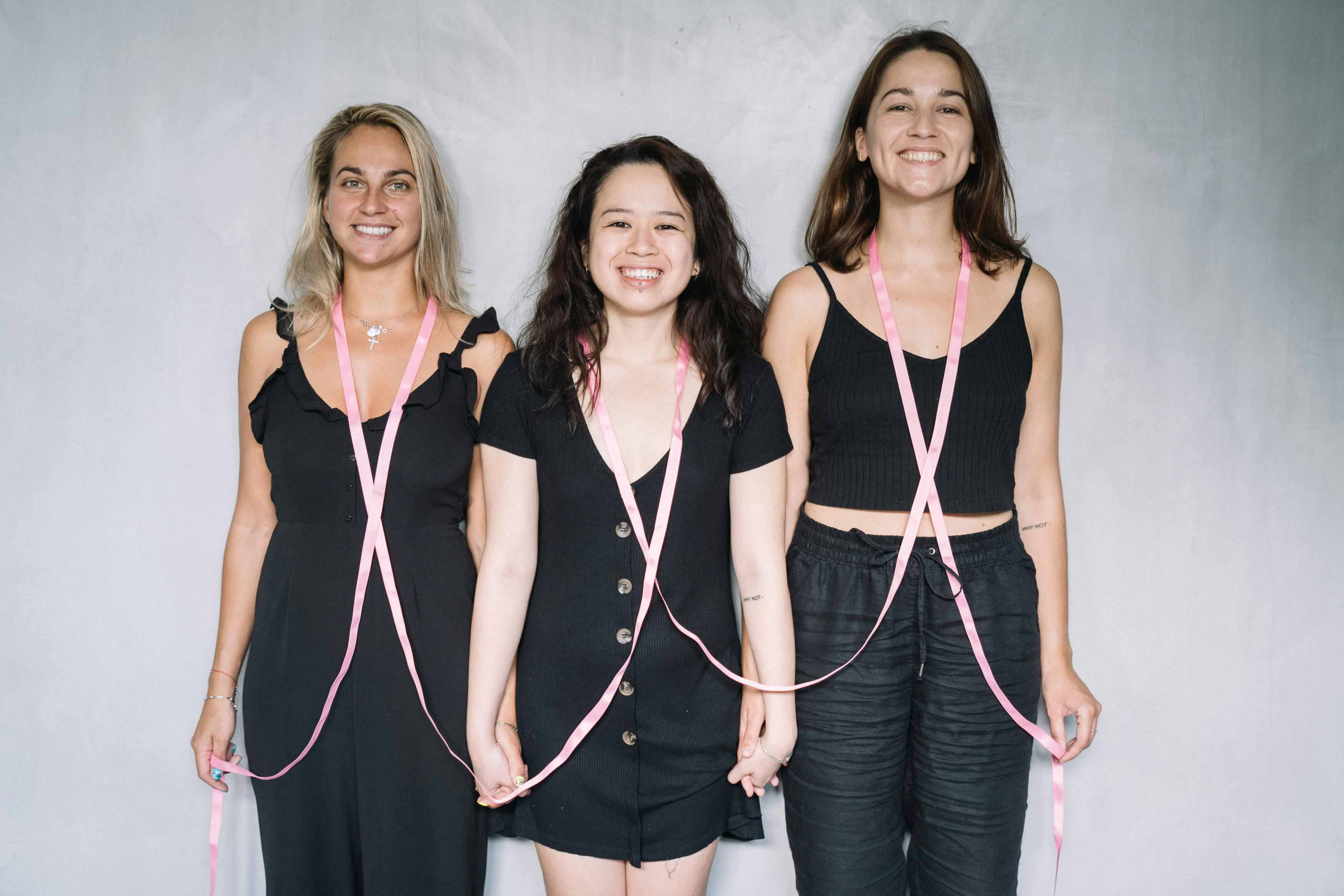 Three women smiling with pink ribbon on them
