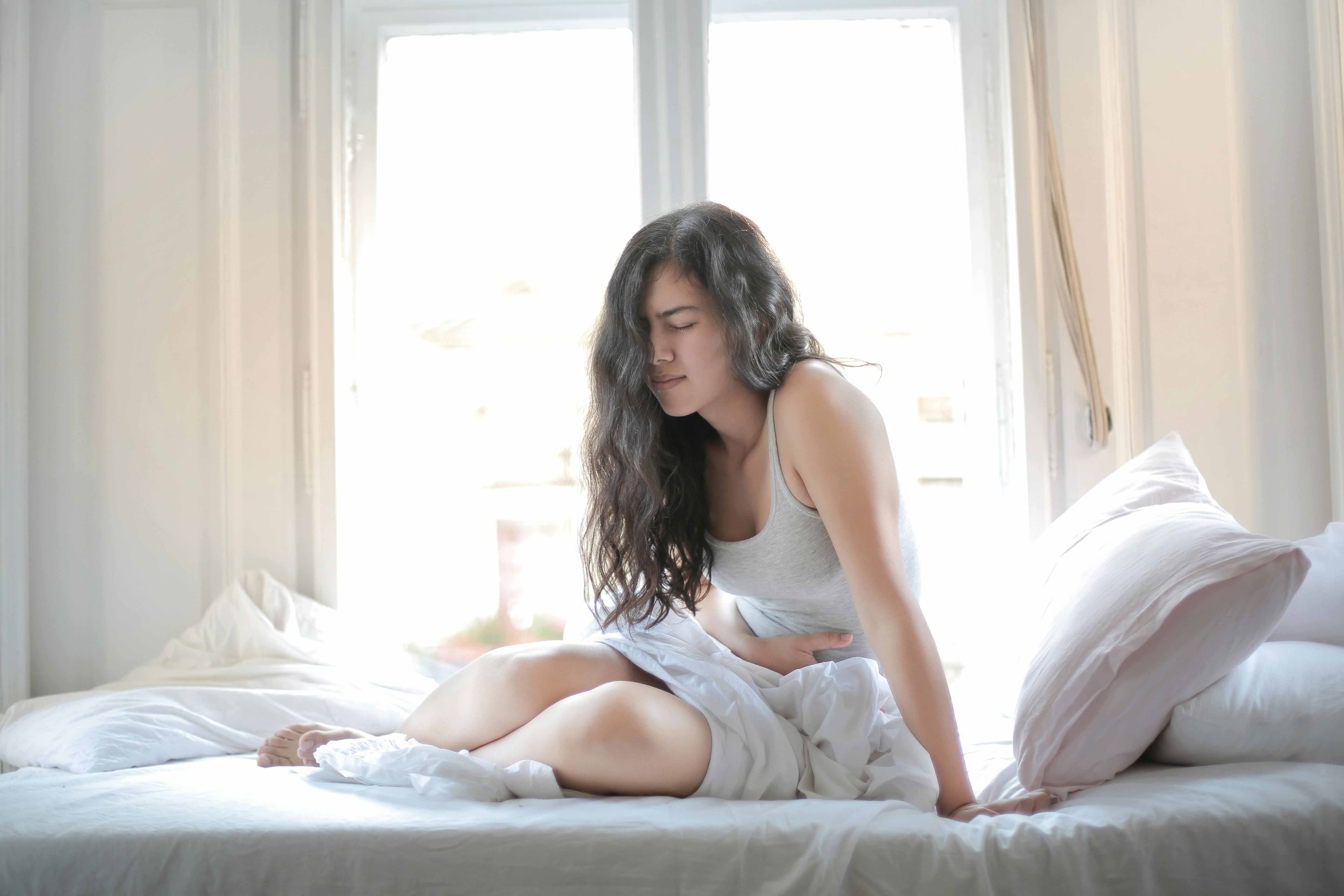 A woman holding her stomach and looking unwell in bed