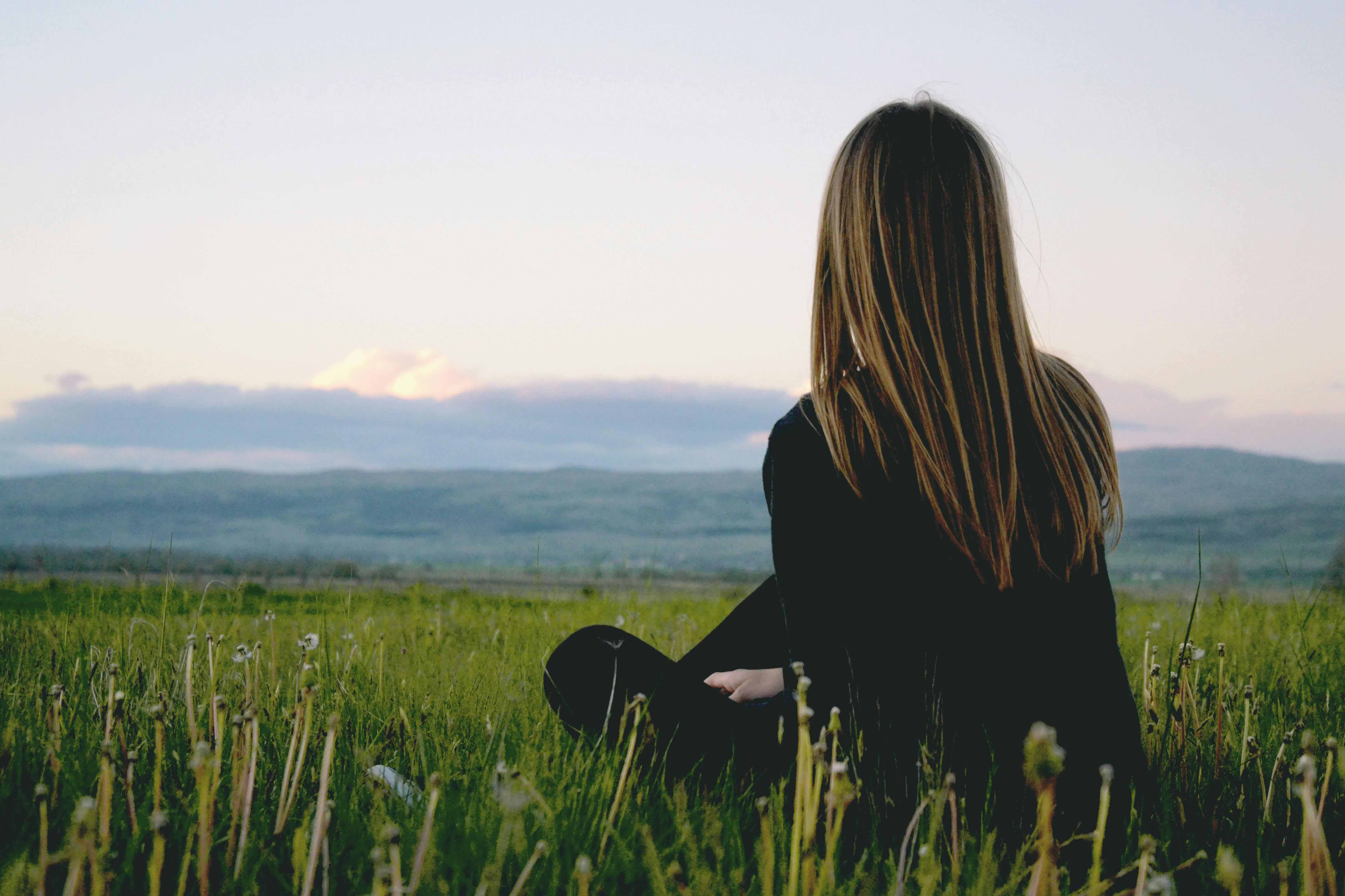 Person looking out into the sunset with mountains and lush grass in the background