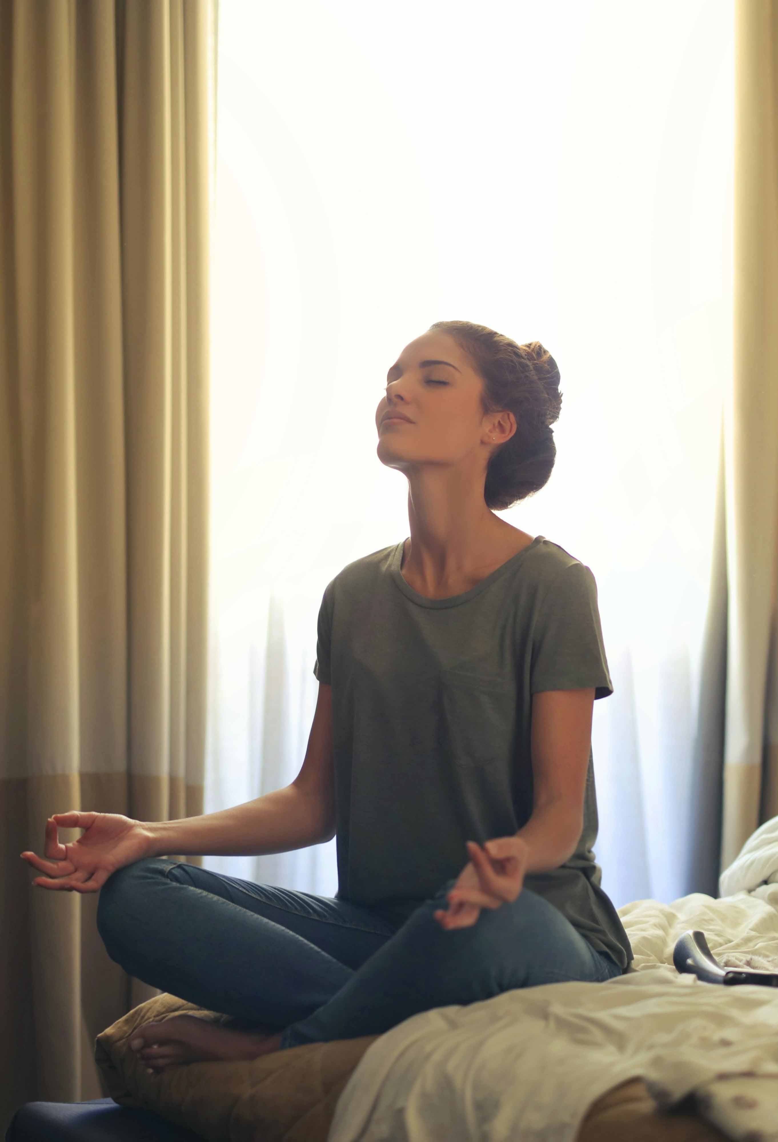 A women sitting cross-legged and meditating on her bed