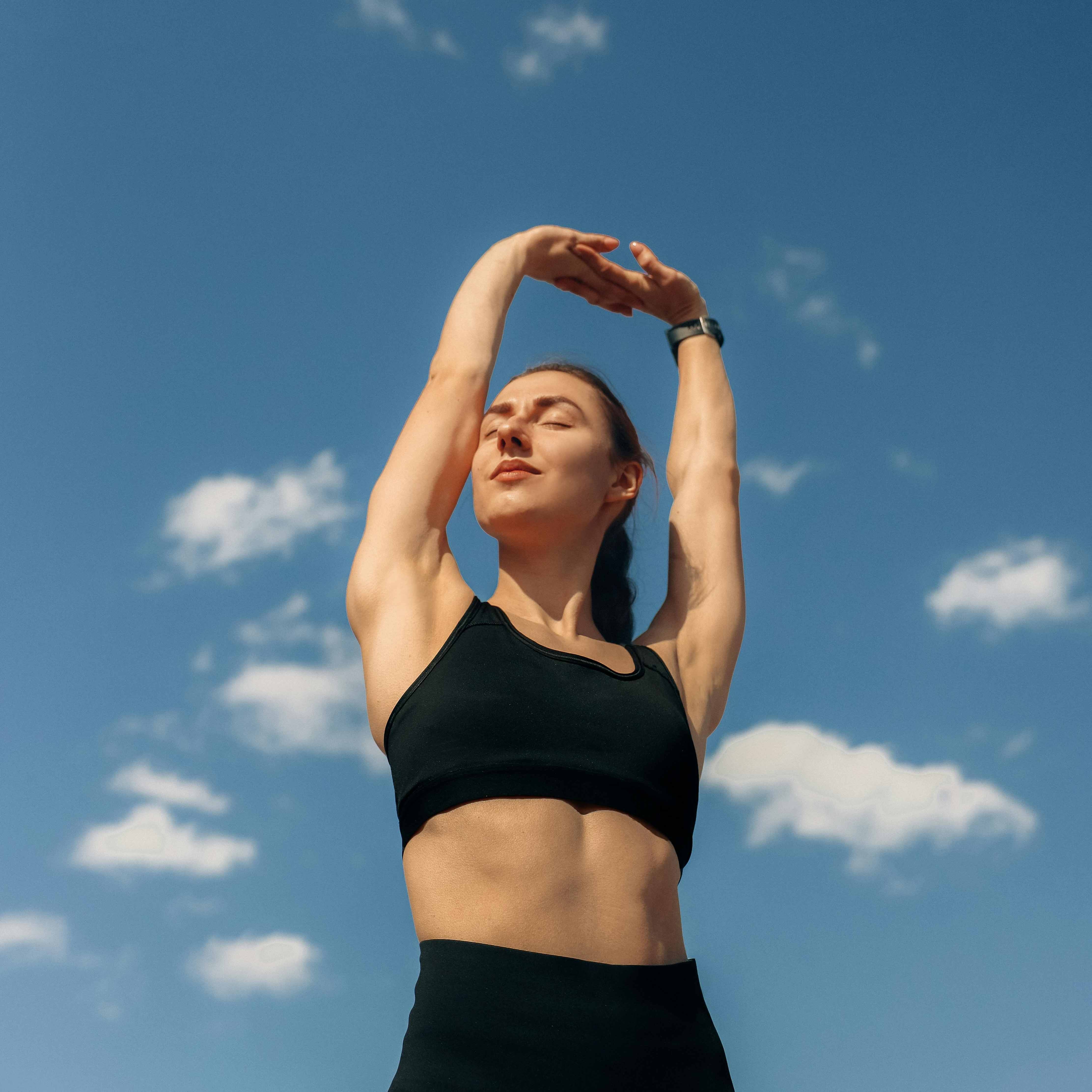 Woman stretching her arms above her head with a beautiful blue sky in the background