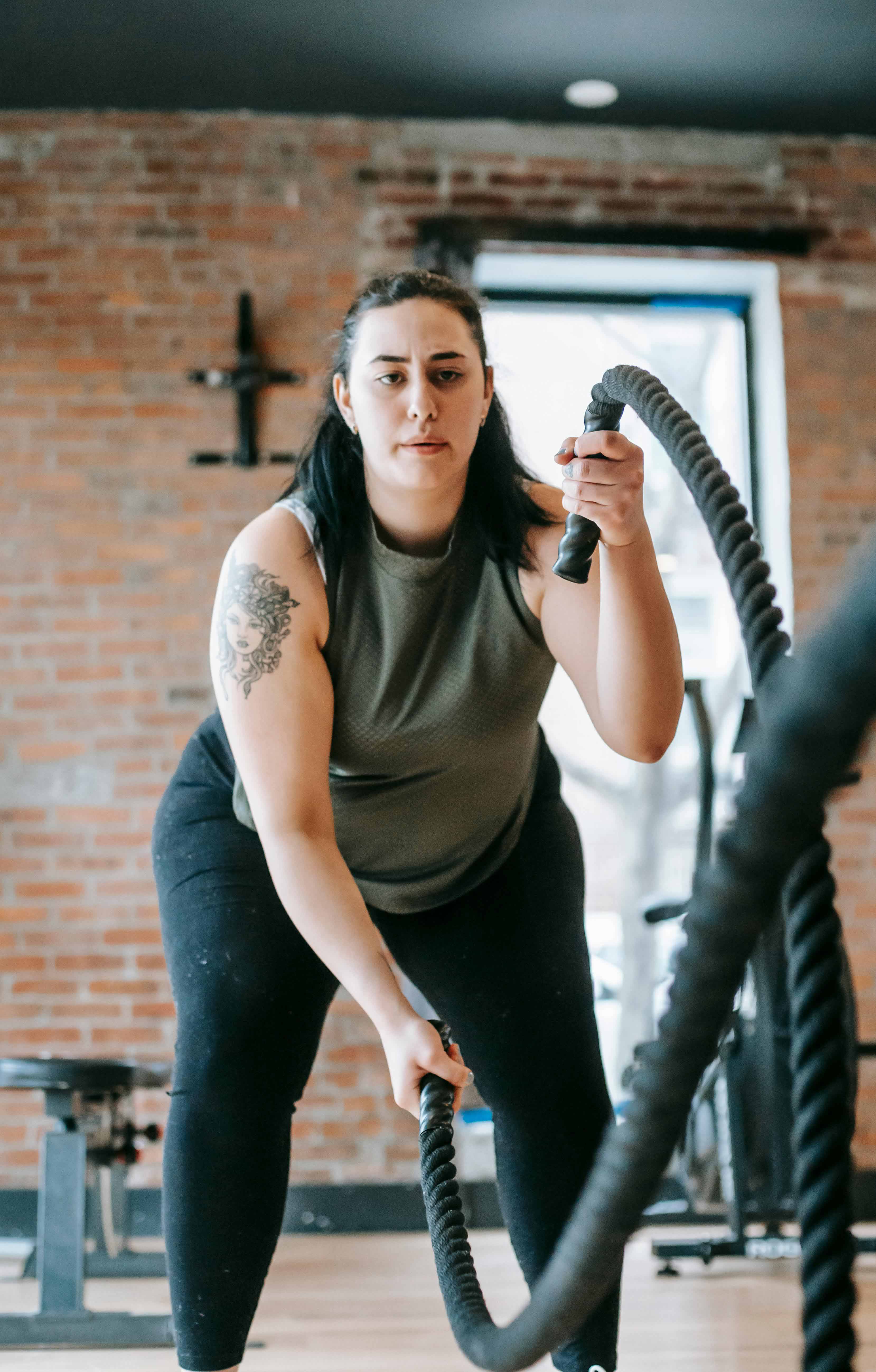 Woman performing a battle rope workout, moving two heavy ropes in an up-and-down motion during an intense fitness session
