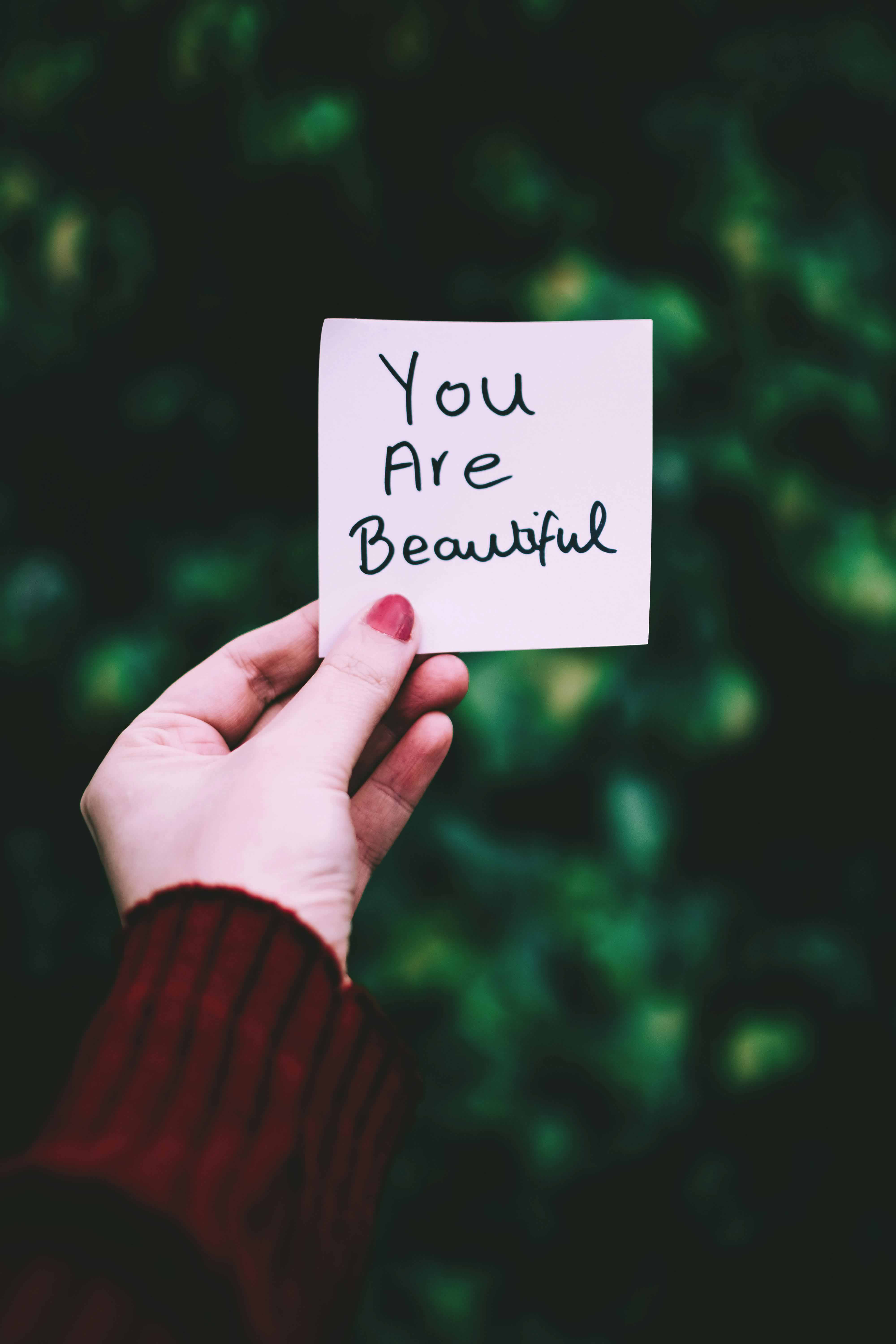 A person holding up a affirmation card that has the text you are beautiful on it