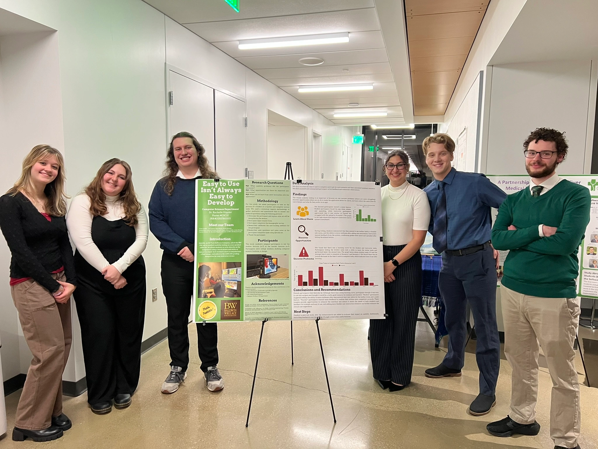 Photo of the UX team standing infront of our UX poster at CEMS